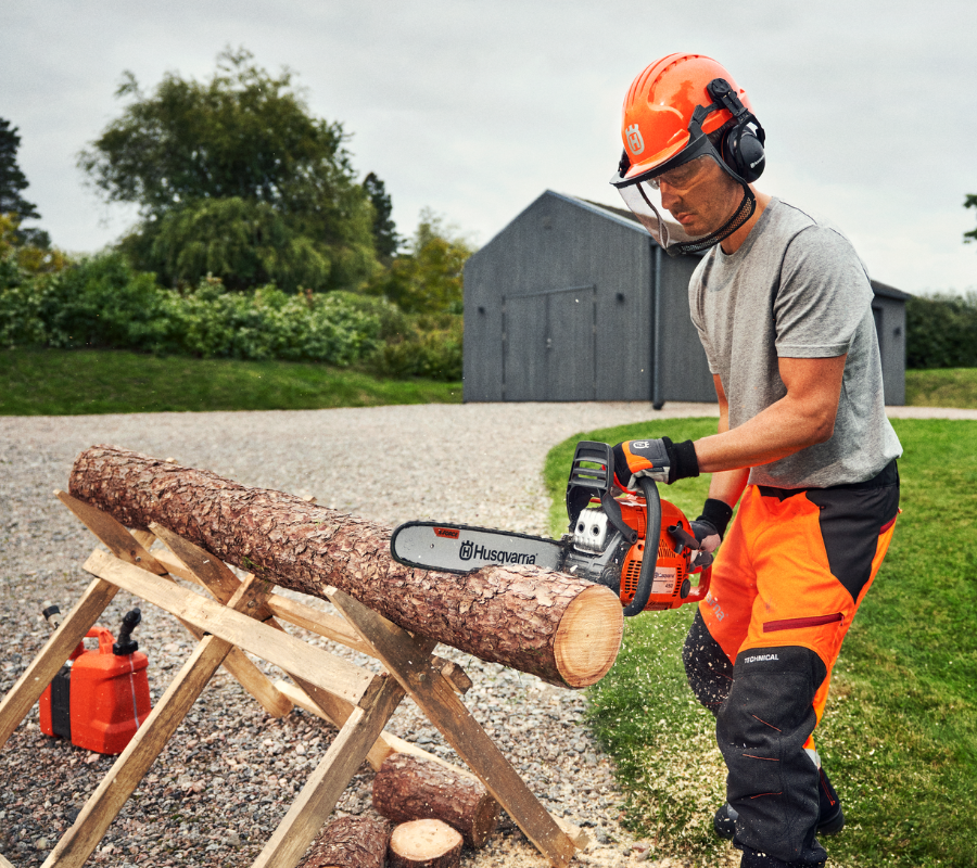 man cutting up log in backyard