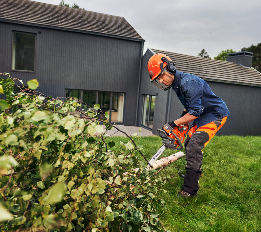 man cutting up log in backyard